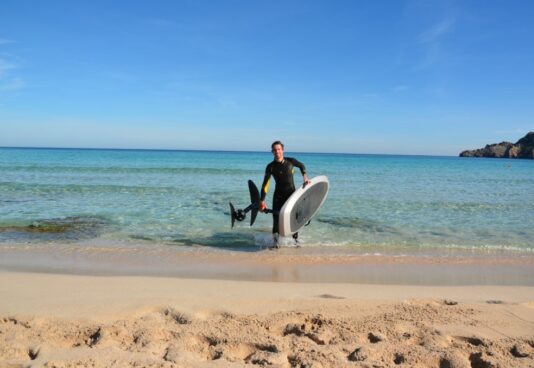 Ein E-Foil-Lehrer der E-Foil Academy Wave Lovers, läuft aus dem Meer auf Mallorca in einer schönen Bucht